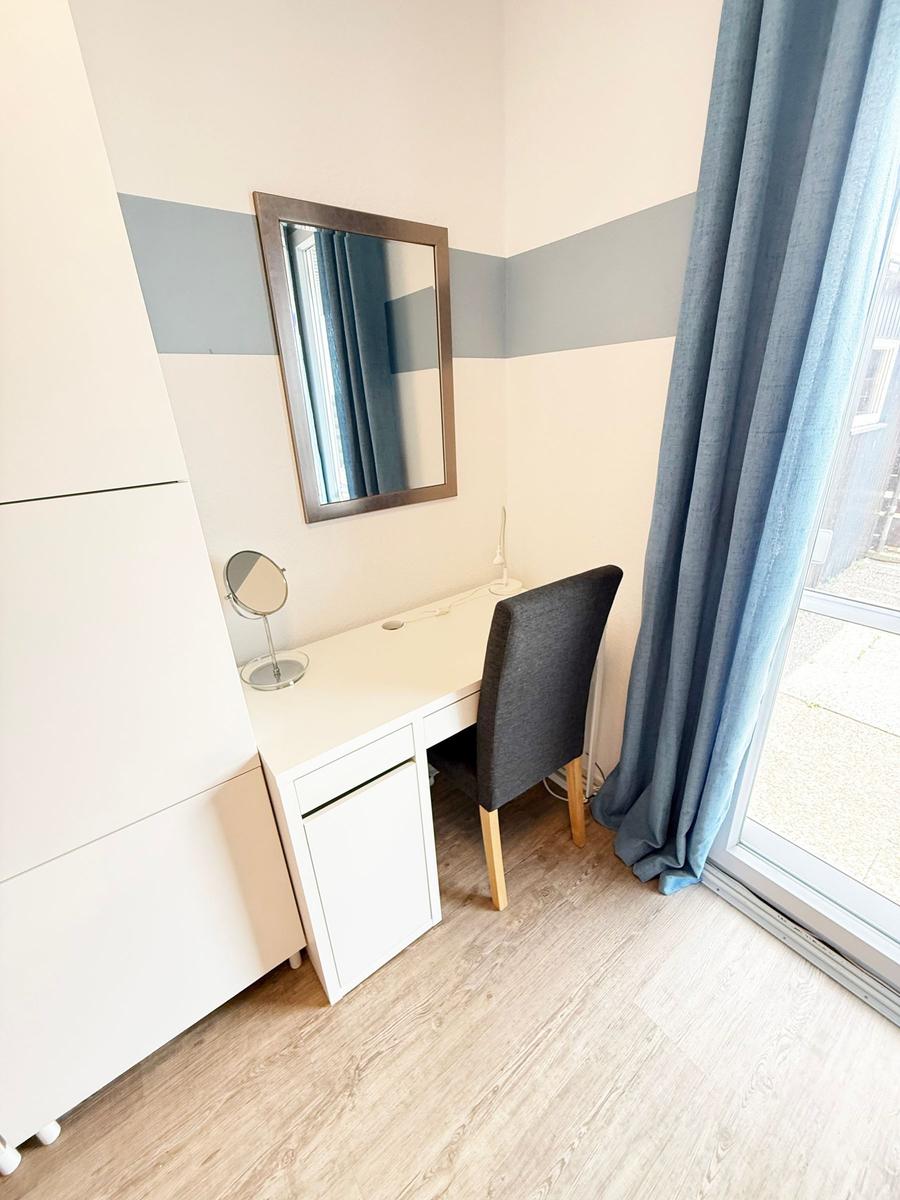 Schreibtisch mit Stuhl, Spiegel und Vorhang an Fenster
