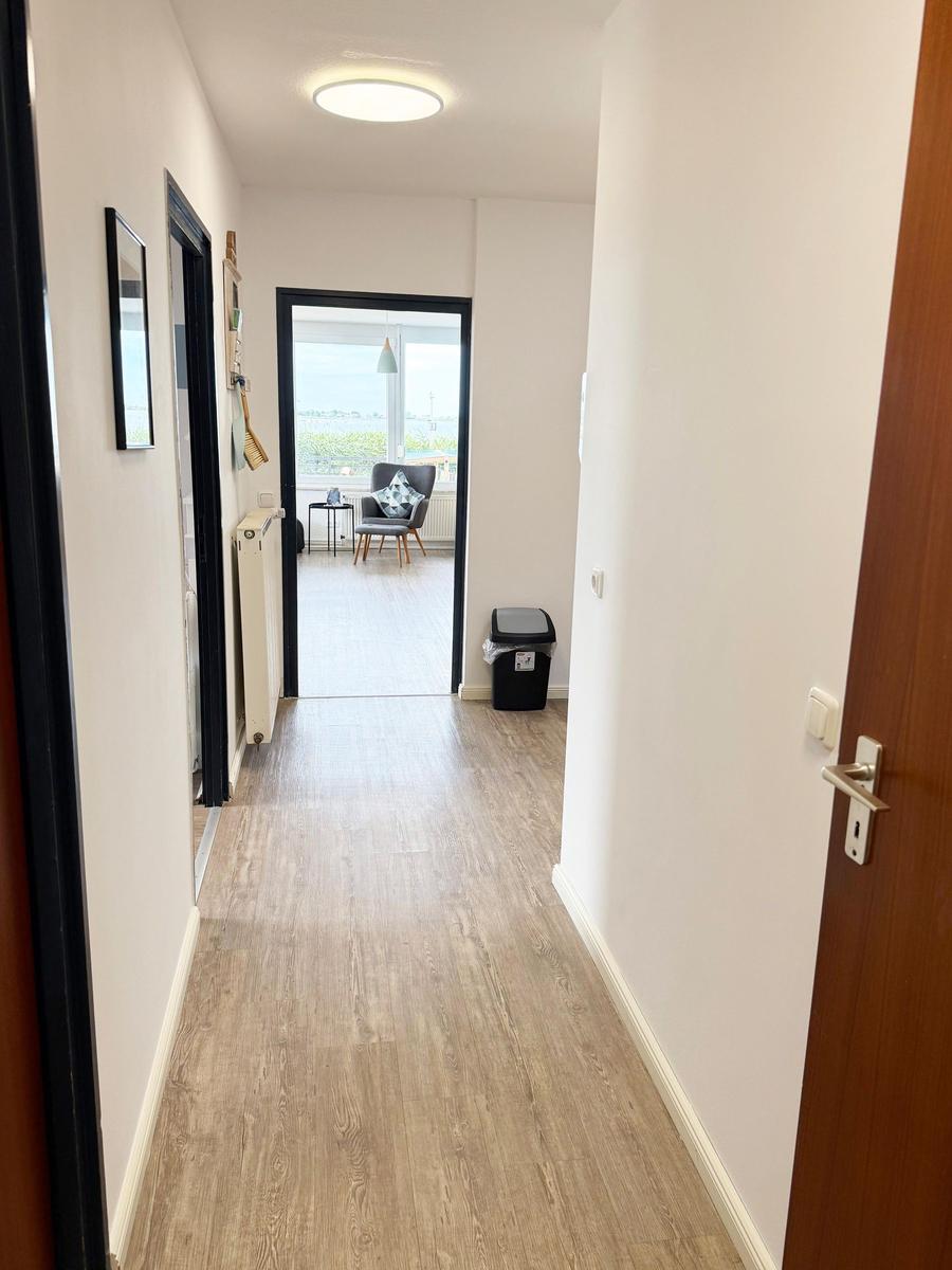Flur mit Holzdielen führt in Wohnzimmer mit Sitzgelegenheit und Fenster.