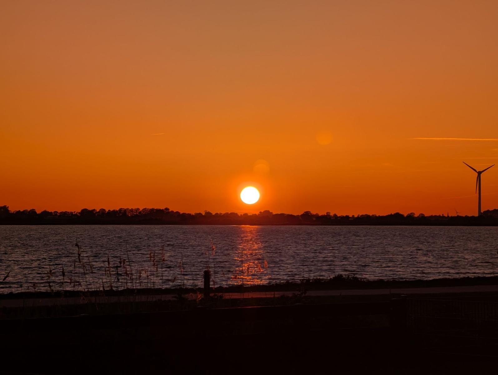 Sonnenuntergang über Wasser mit Windrad am Horizont.