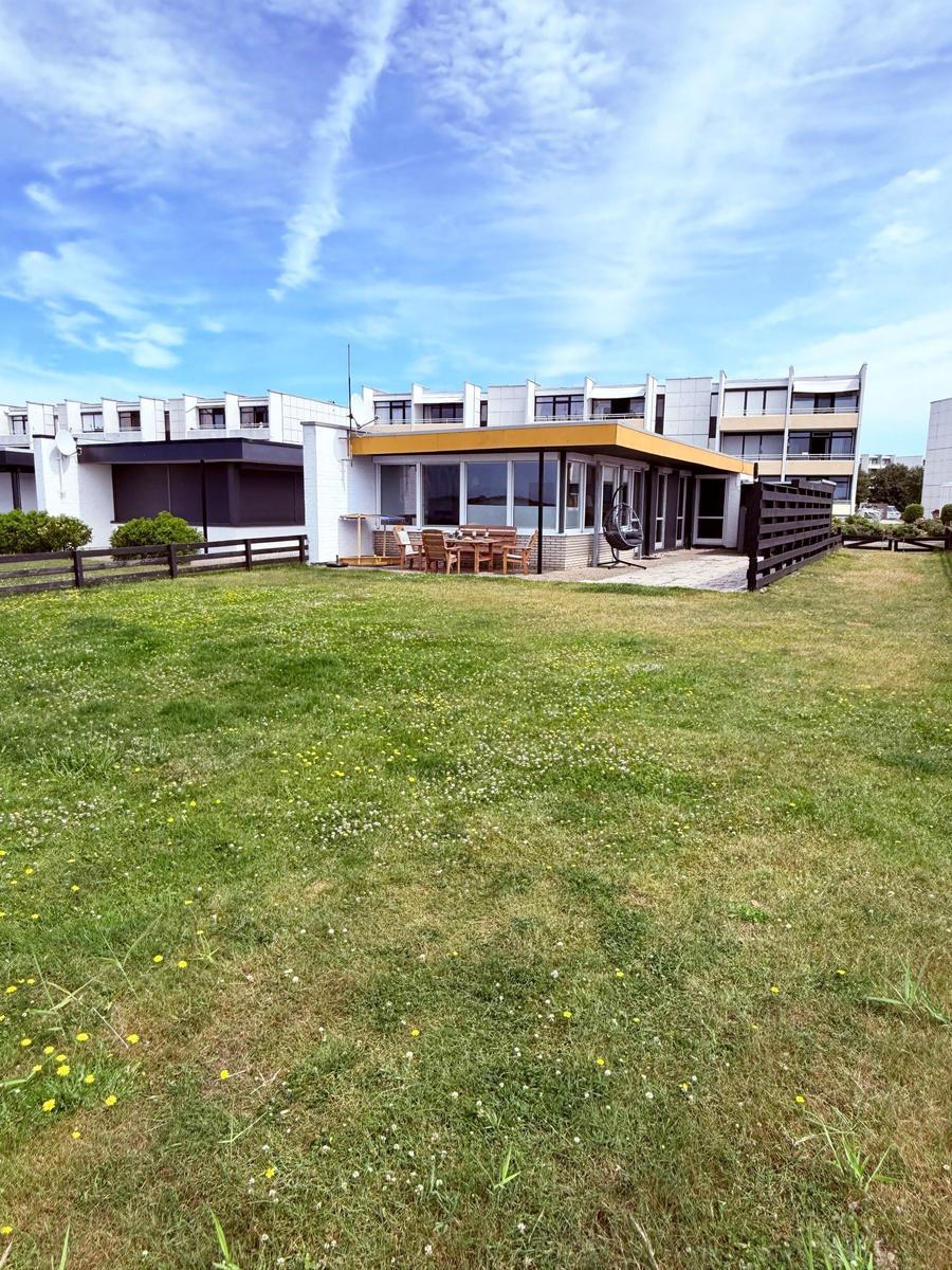 Haus mit Terrasse, Garten und Sitzgelegenheiten unter blauem Himmel.