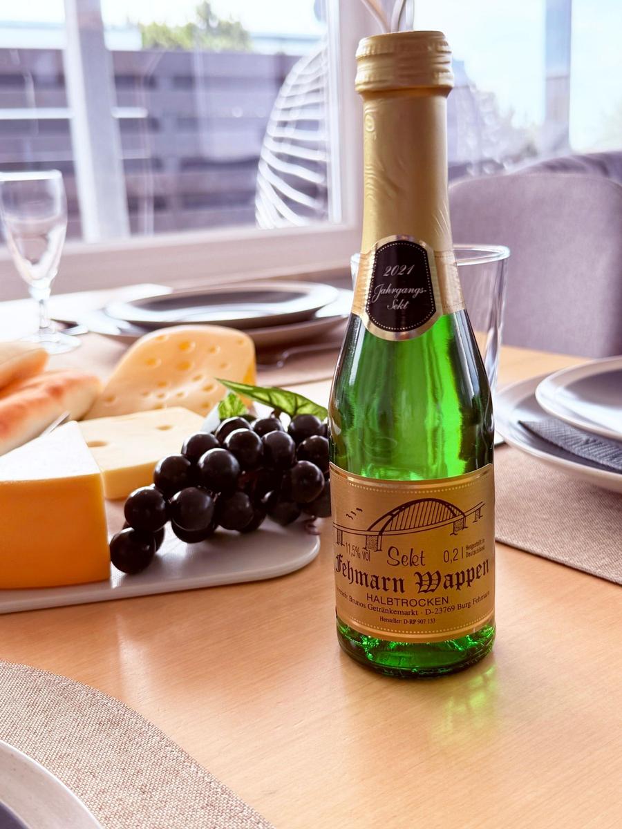 Auf dem Tisch steht eine Sektflasche neben Käse und Trauben.