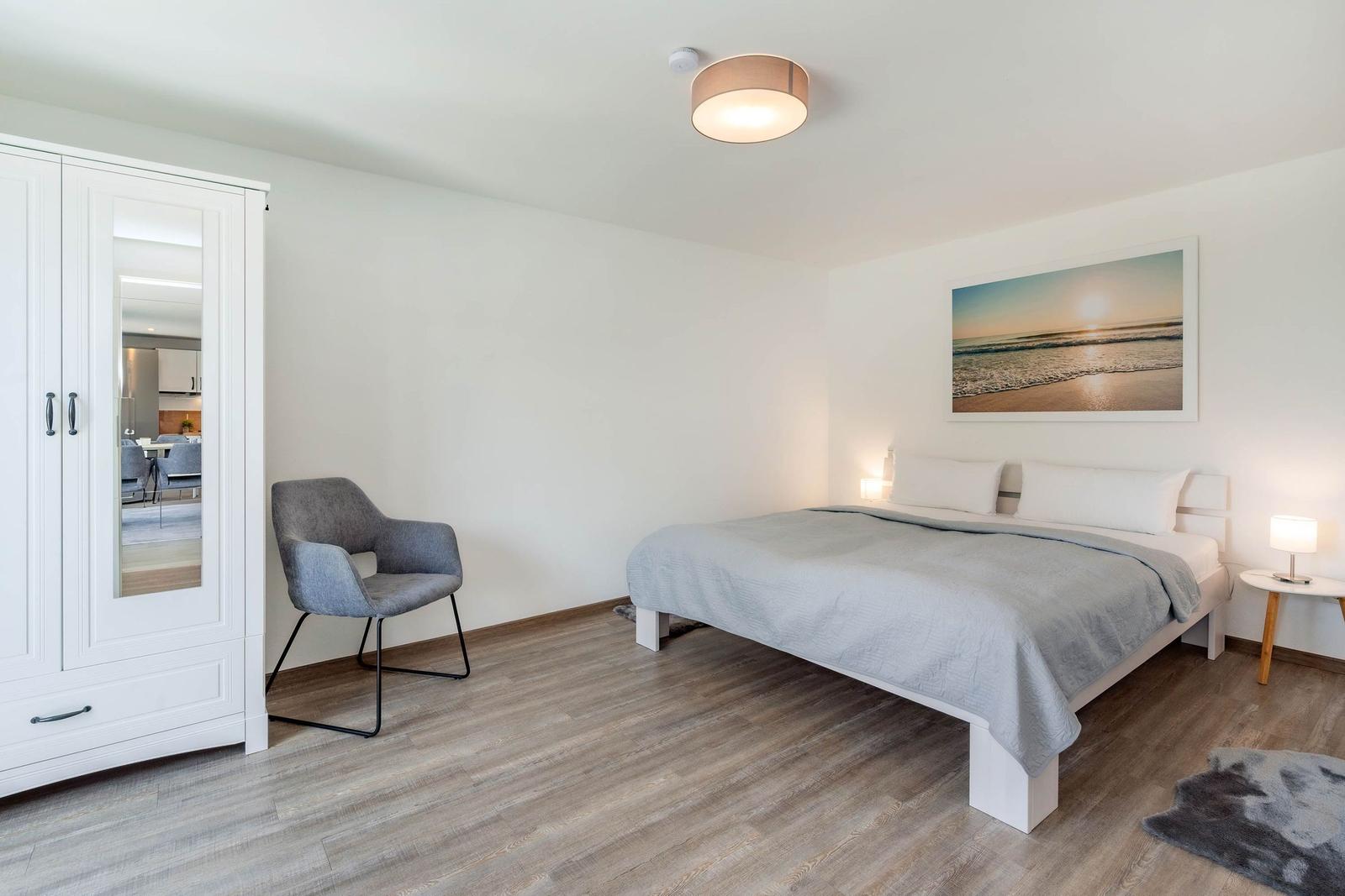 Schlafzimmer mit Bett, Schreibtischstuhl und Kleiderschrank. Wandbild zeigt Strand.