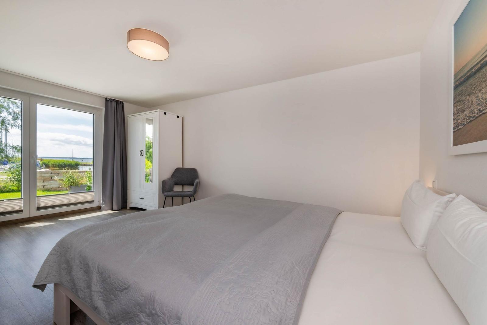 Schlafzimmer mit Doppelbett, Schrank und Blick auf Außenbereich.