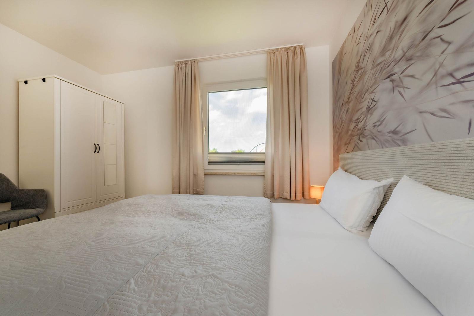 Schlafzimmer mit Bett, Kleiderschrank und Fenster mit Vorhängen.