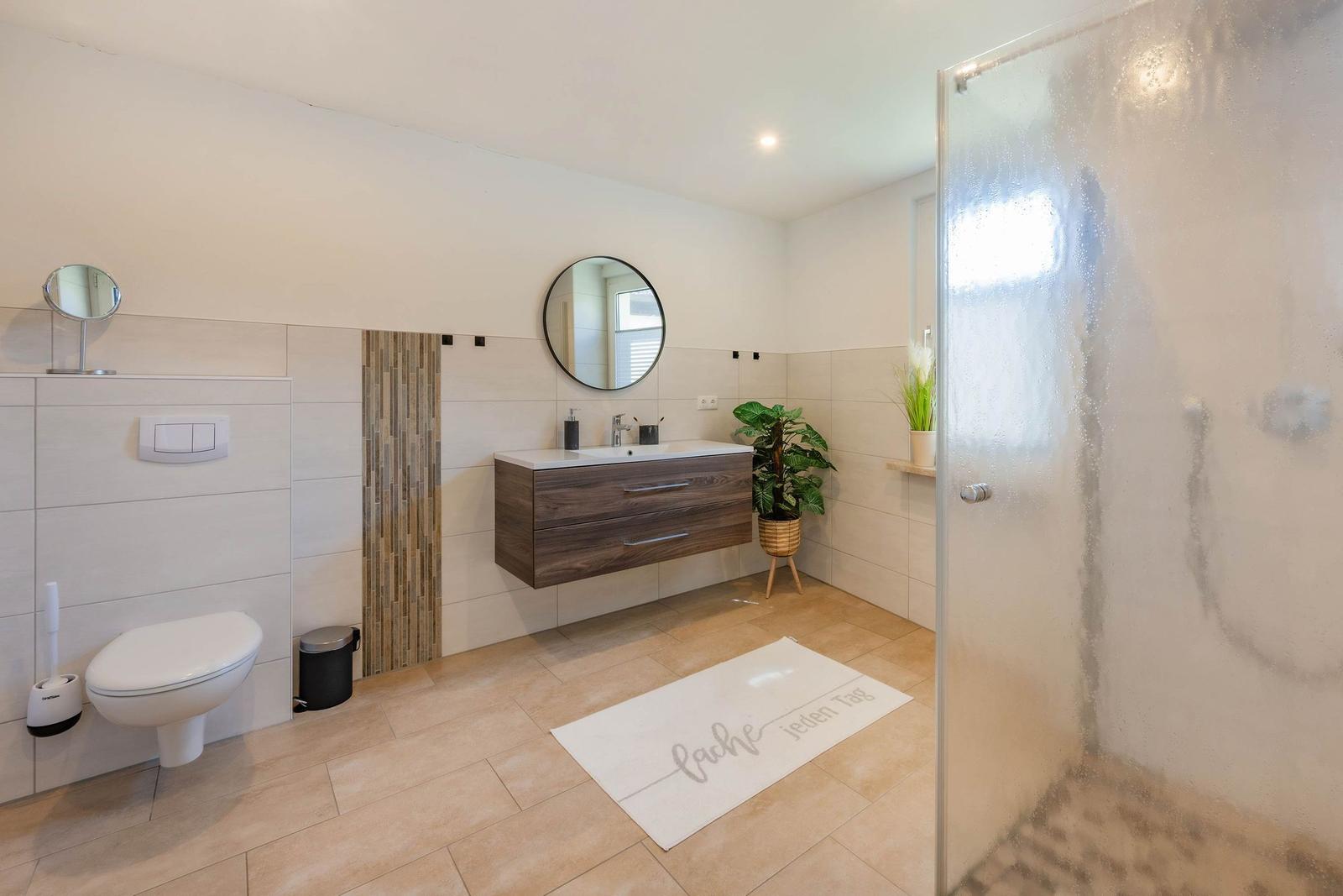 Badezimmer mit Dusche, Waschbecken und Toilette. Boden- und Wandfliesen.
