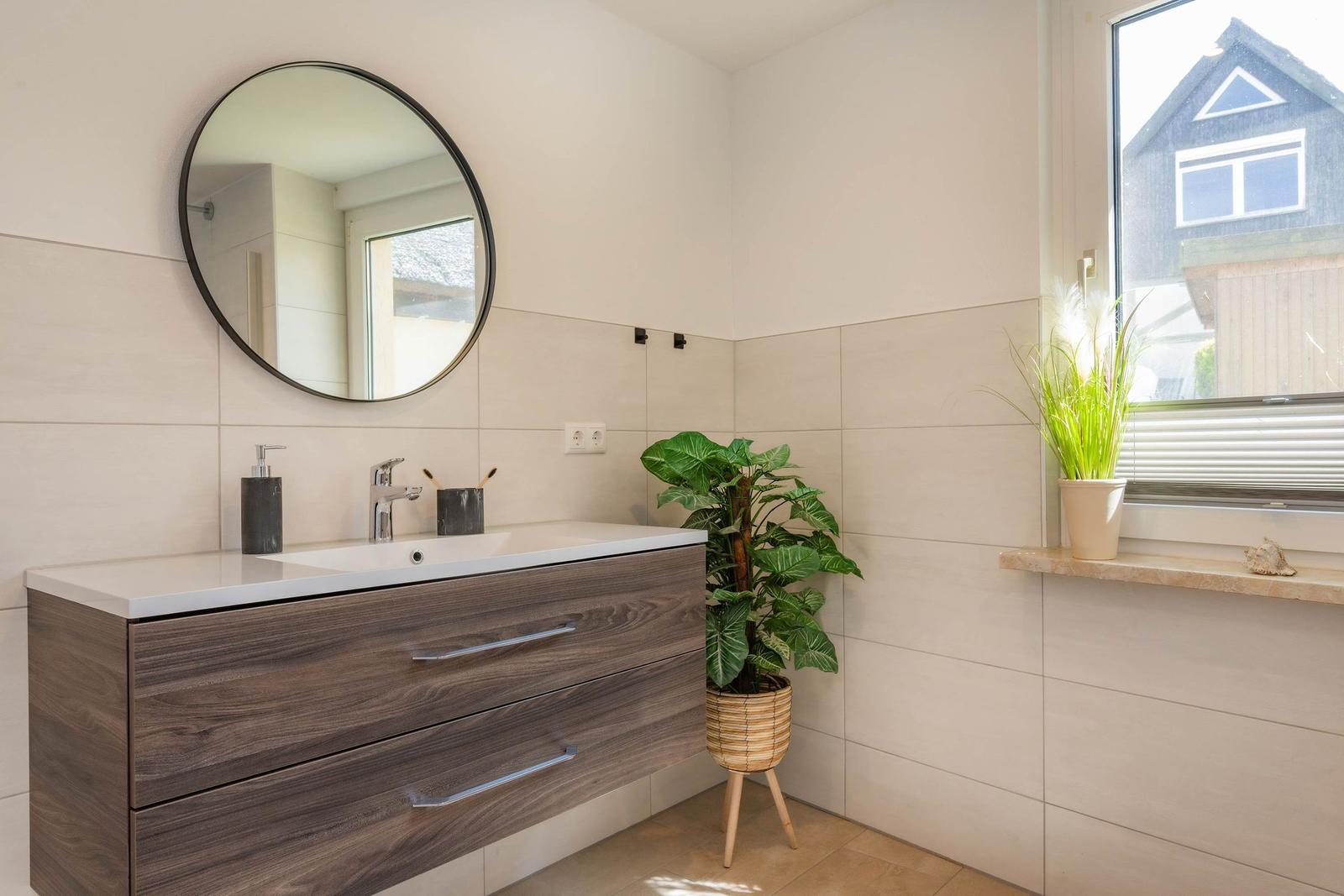 Bad mit Waschbecken, Spiegel und Pflanzen an Fensterbank.