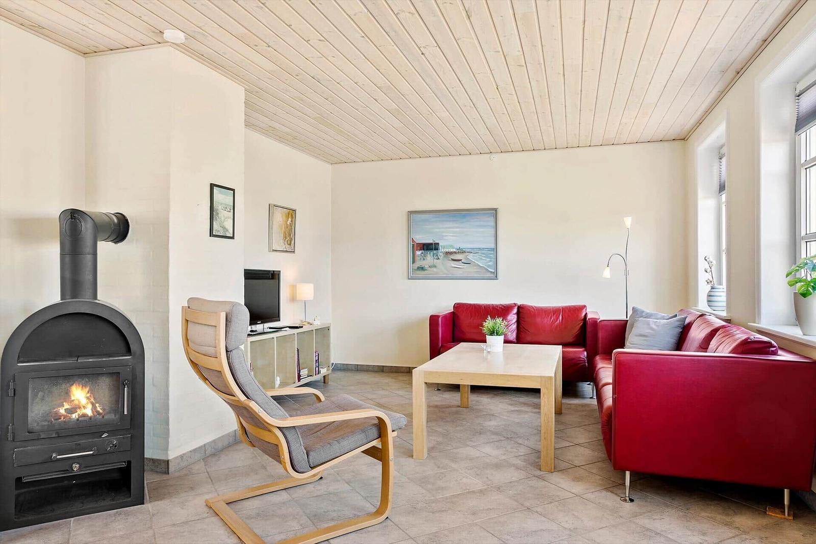 Wohnzimmer mit rotem Sofa, Holztisch und Kaminofen. Decke aus Holz, Wandbild und Fenster.