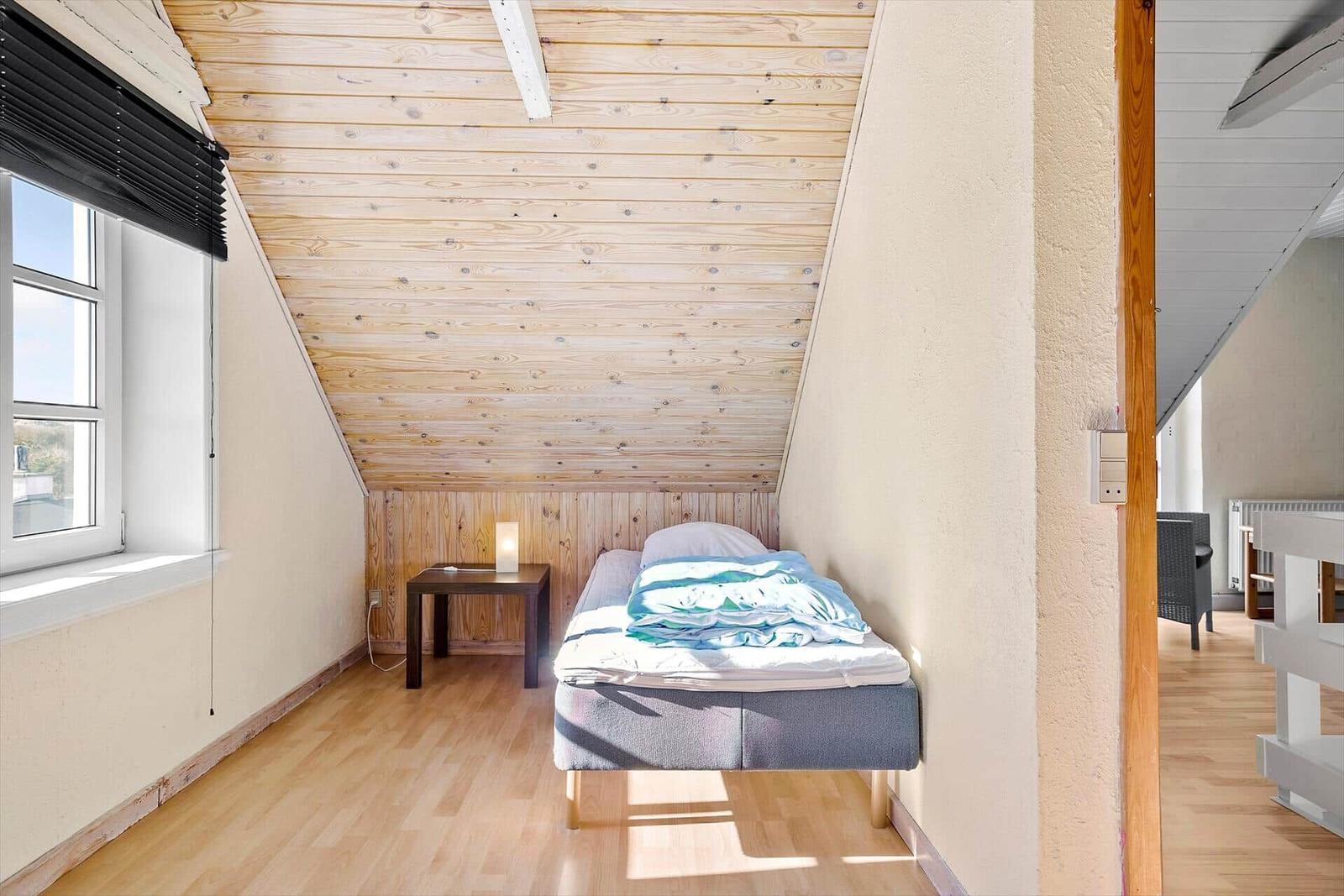 Ein Schlafzimmer mit Dachschräge, Holzboden und einem Bett mit blauer Bettwäsche.