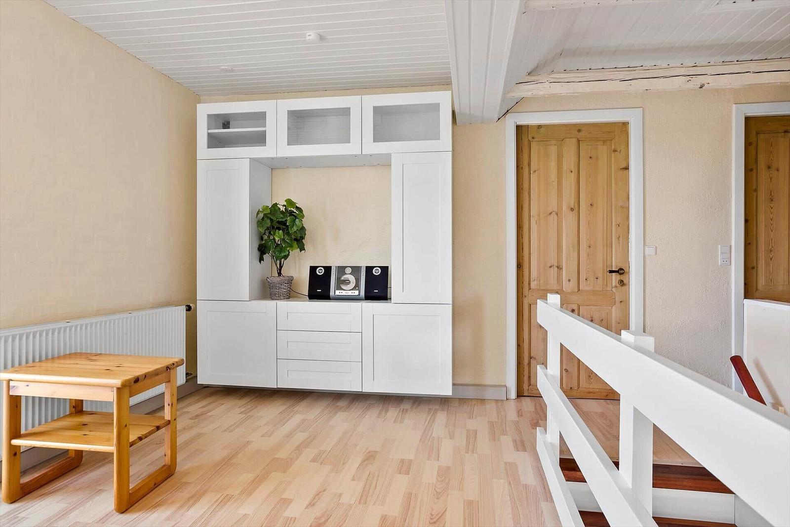 Raum mit weißem Schrank, Holztisch und Holzfußboden. Tür und Geländer sind sichtbar.