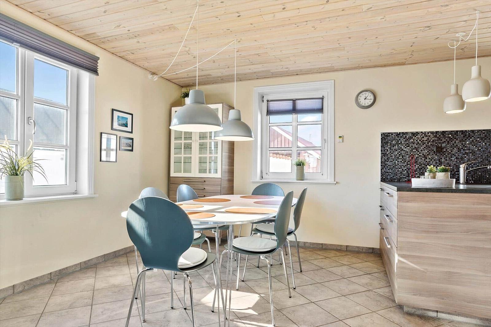 Essbereich mit Tisch, Stühlen und Küchenzeile unter Holzdecke.