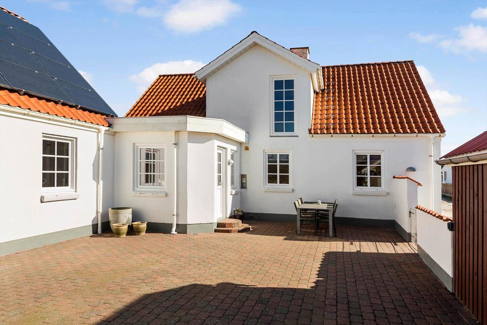 Weiße Villa mit rotem Dach und gepflastertem Hof. Tisch und Stühle stehen im Freien.