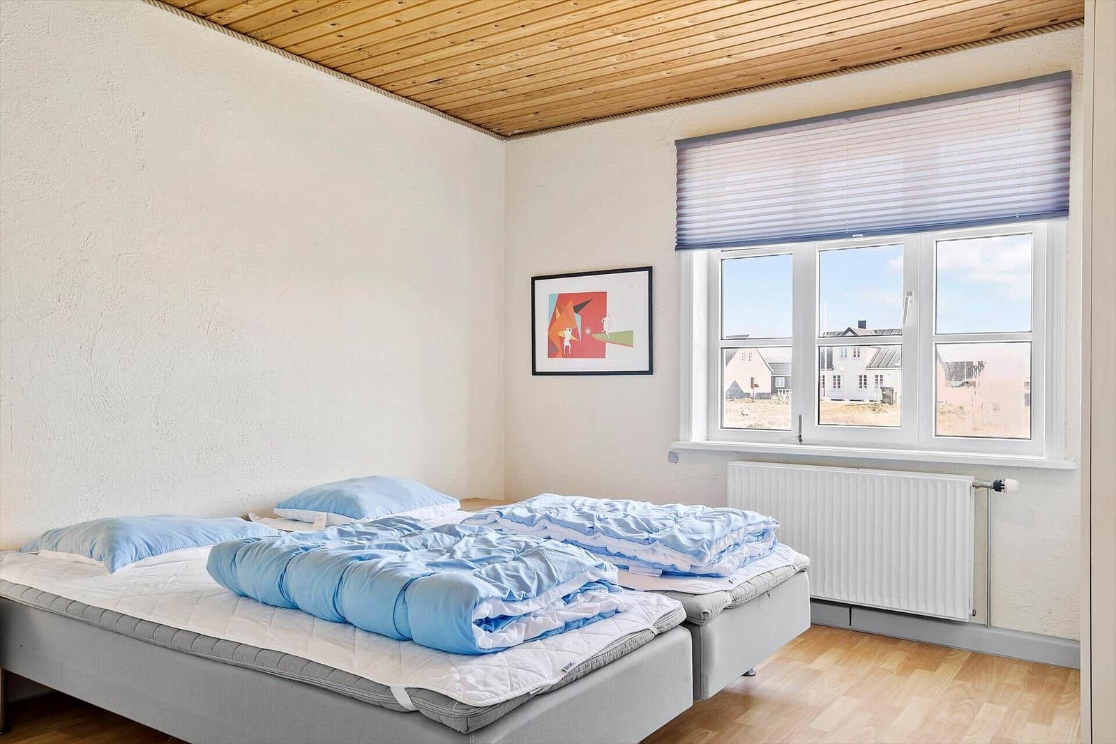Schlafzimmer mit Doppelbett, Holzboden und Fenster mit Blick auf Außenbereich.