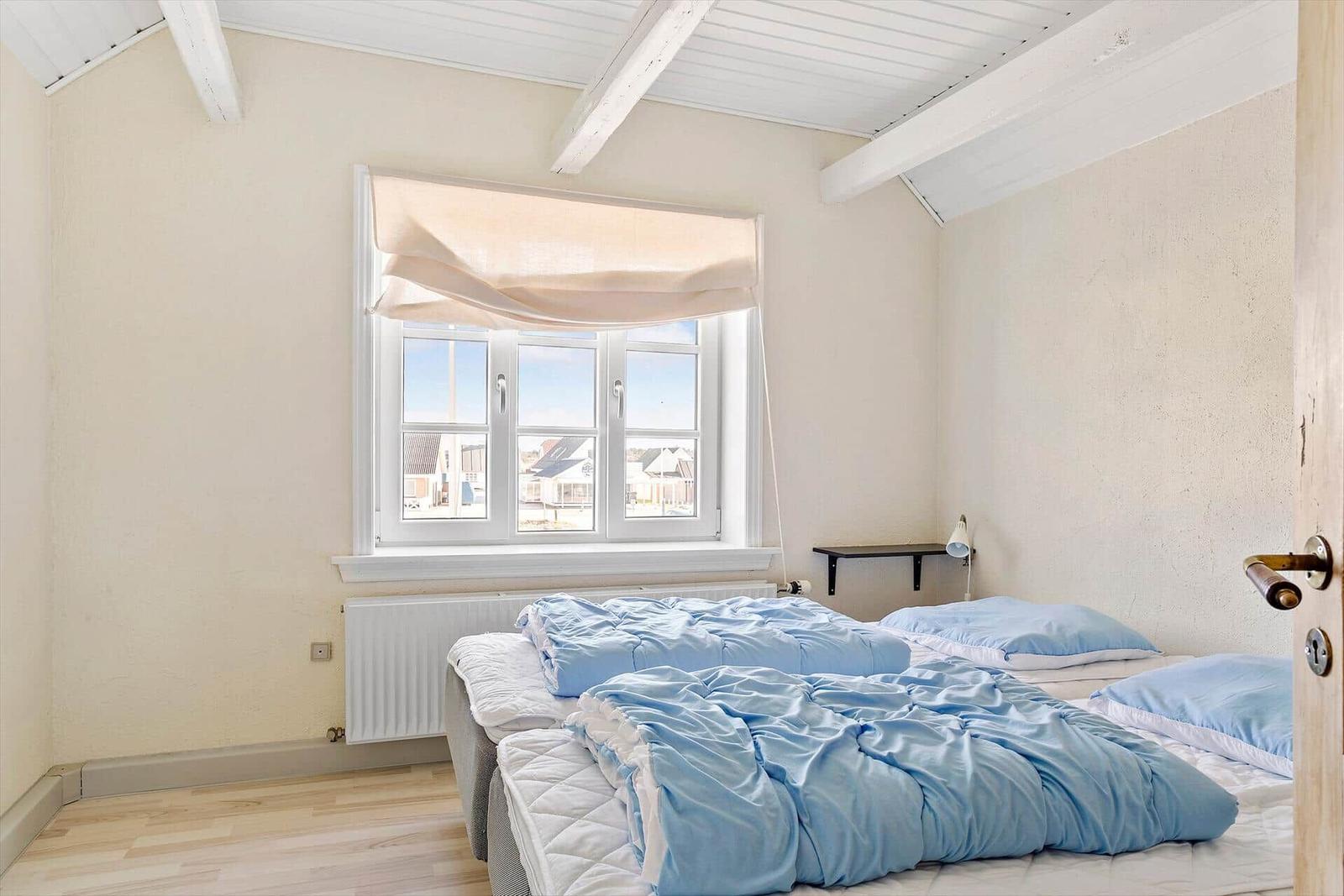 Schlafzimmer mit Bett, Fenster und Holzbalken an der Decke.