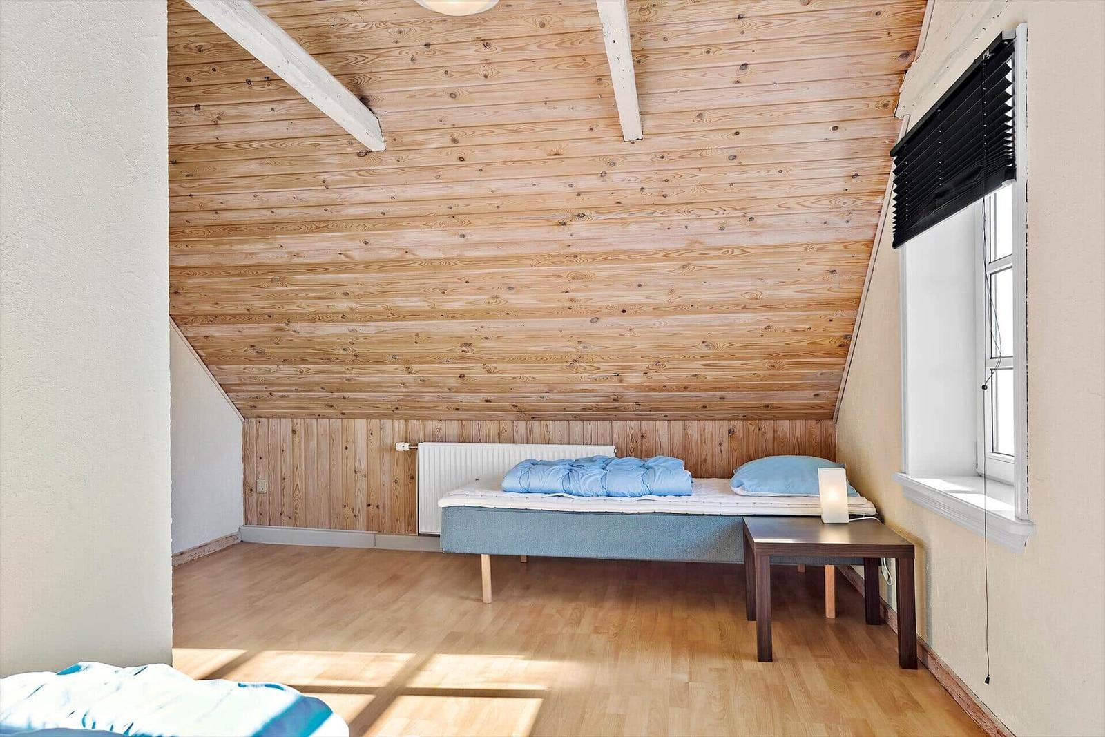 Schlafzimmer mit Holzdecke, Bett und Tisch. Fenster mit Jalousie.