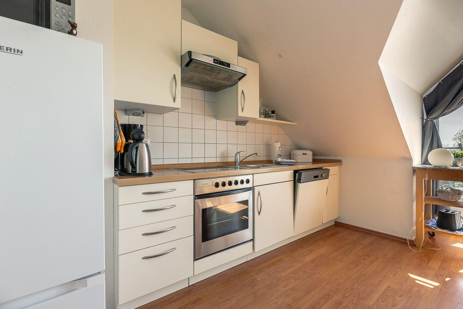 Küche mit Kühlschrank, Herd, Spüle und Geschirrspüler unter schrägem Dach.