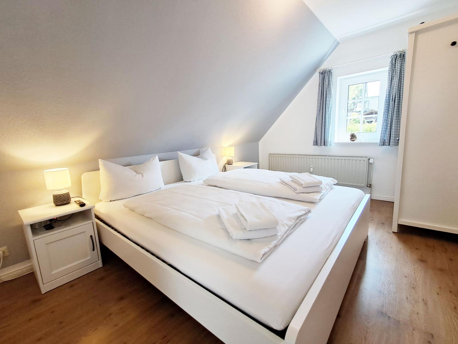 Schlafzimmer mit Doppelbett, Nachttisch und Fenster mit Vorhängen.