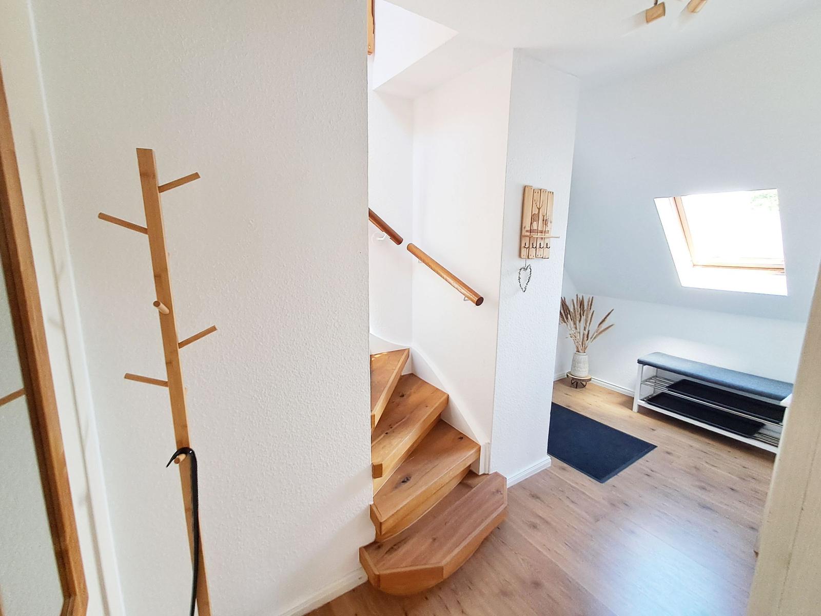 Holztreppe führt nach oben. Wandhaken und Fenster sind sichtbar.