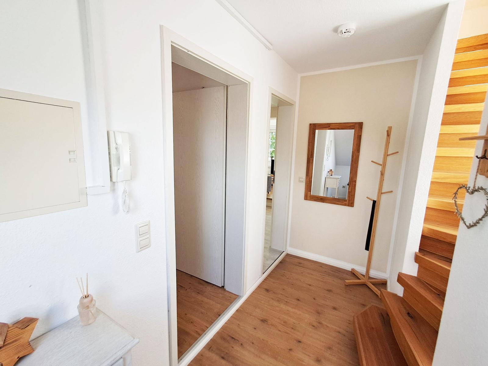 Eingangsbereich mit Holzboden, Spiegel, Kleiderständer und Treppe.
