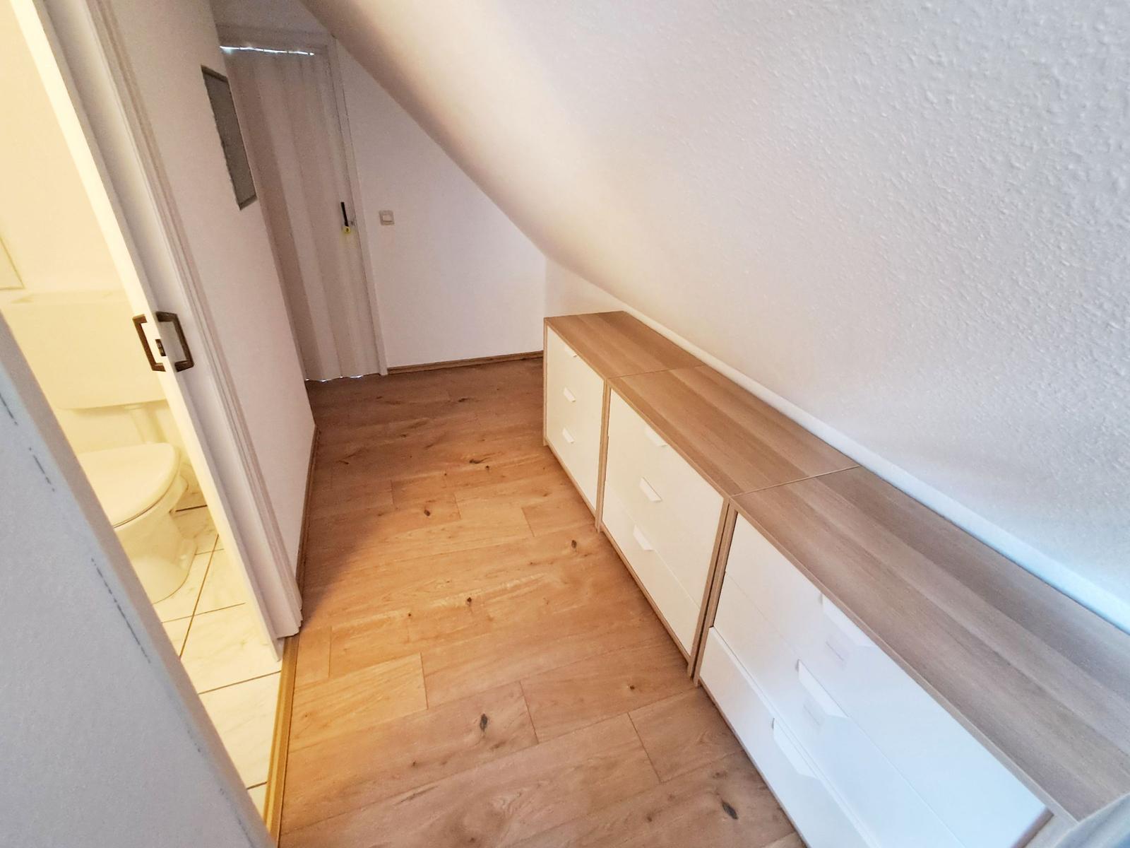 Schlafzimmer mit Holzboden und Schrank unter Dachschräge. Toilettenbereich ist angrenzend.