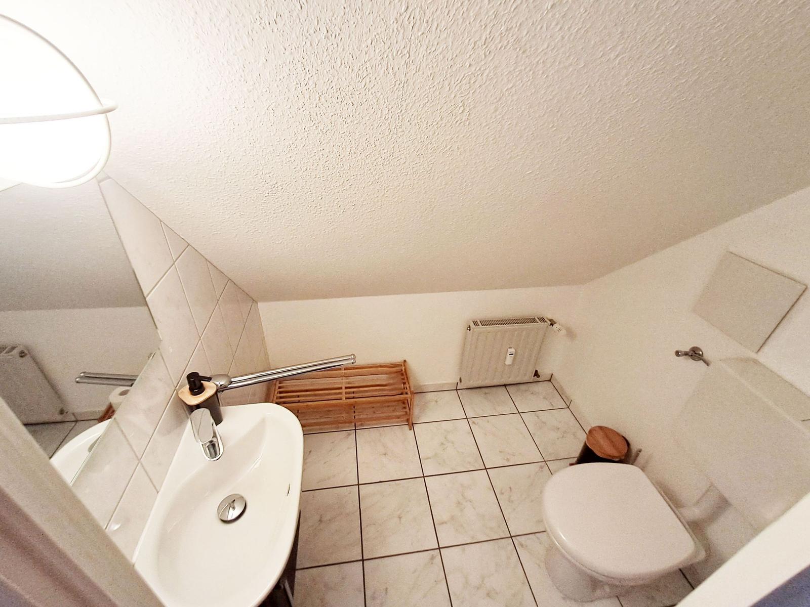 Badezimmer mit Toilette, Waschbecken und Dusche. Fliesenboden und Spiegel.