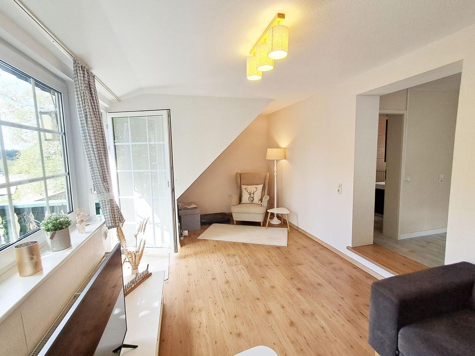 Wohnzimmer mit Holzboden, Fenster, Sessel und Lampen.