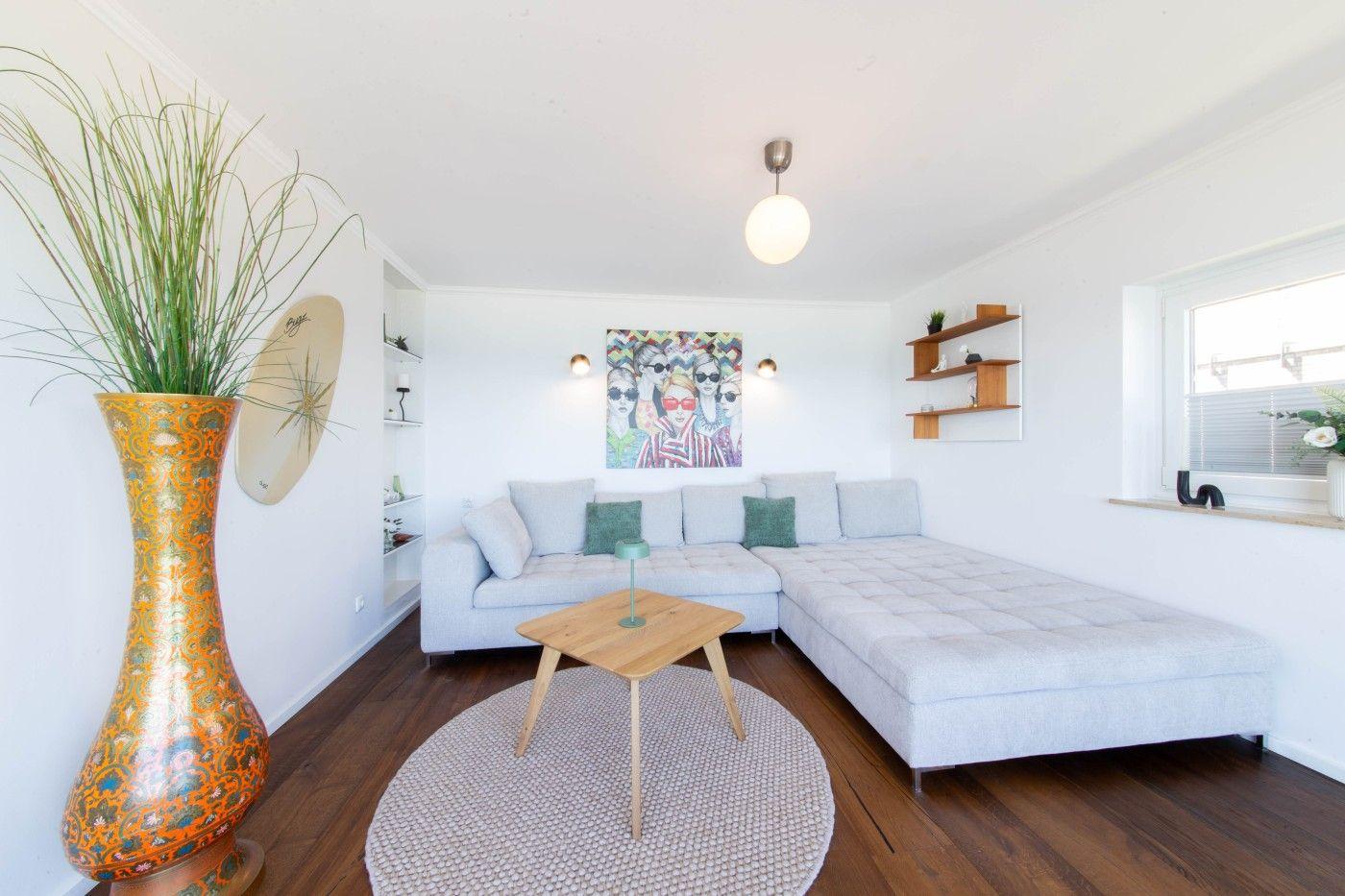 Wohnzimmer mit grauem Sofa, Holztisch und großer Vase.