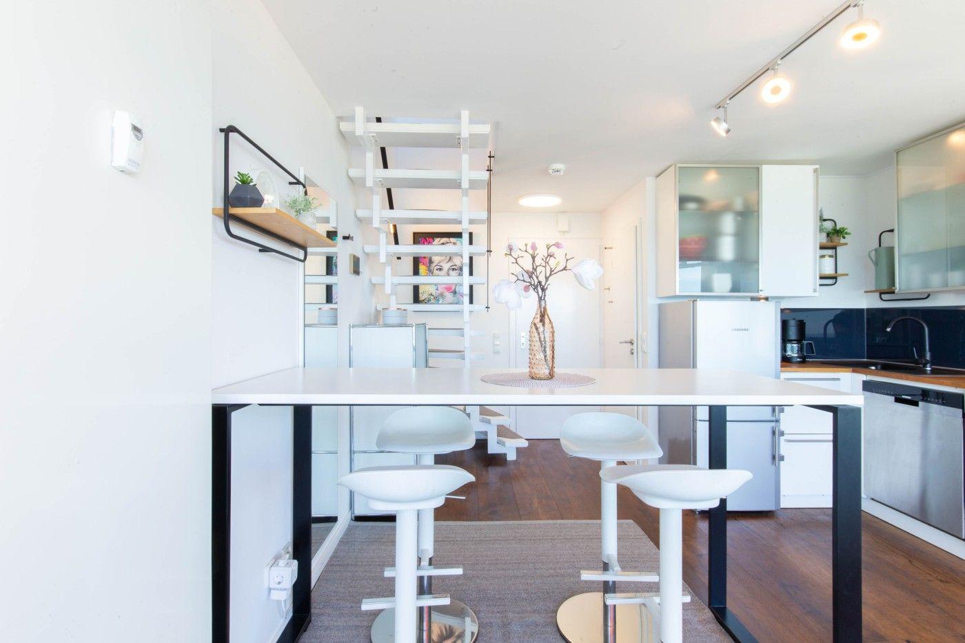 Moderne Küche mit Esstisch, weißen Barhockern und einer Treppe.