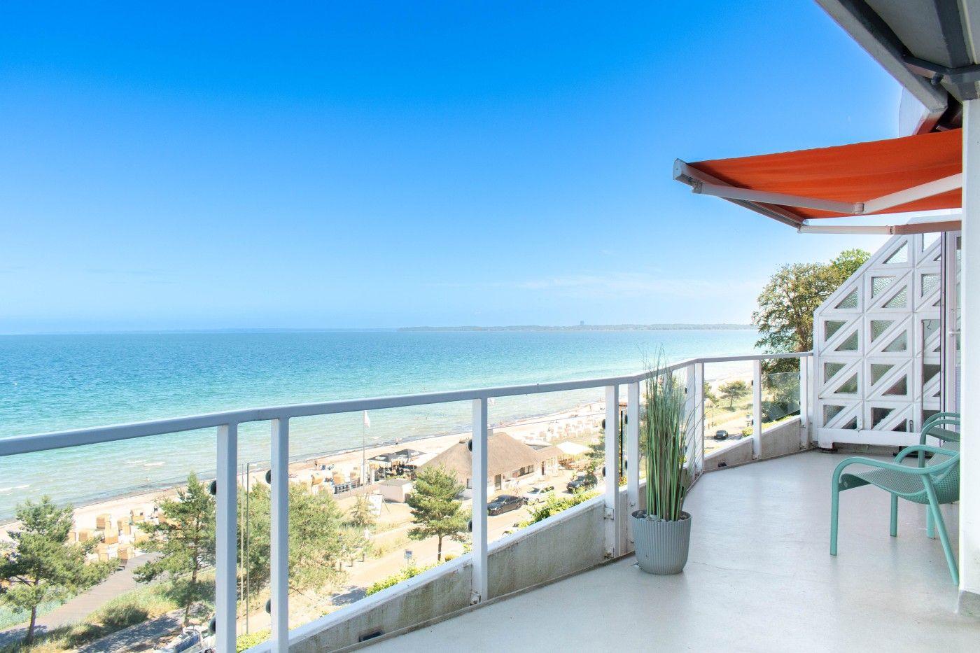 Terrasse mit Blick auf das Meer und Strand. Orange Markise, grüne Stühle und Pflanze.