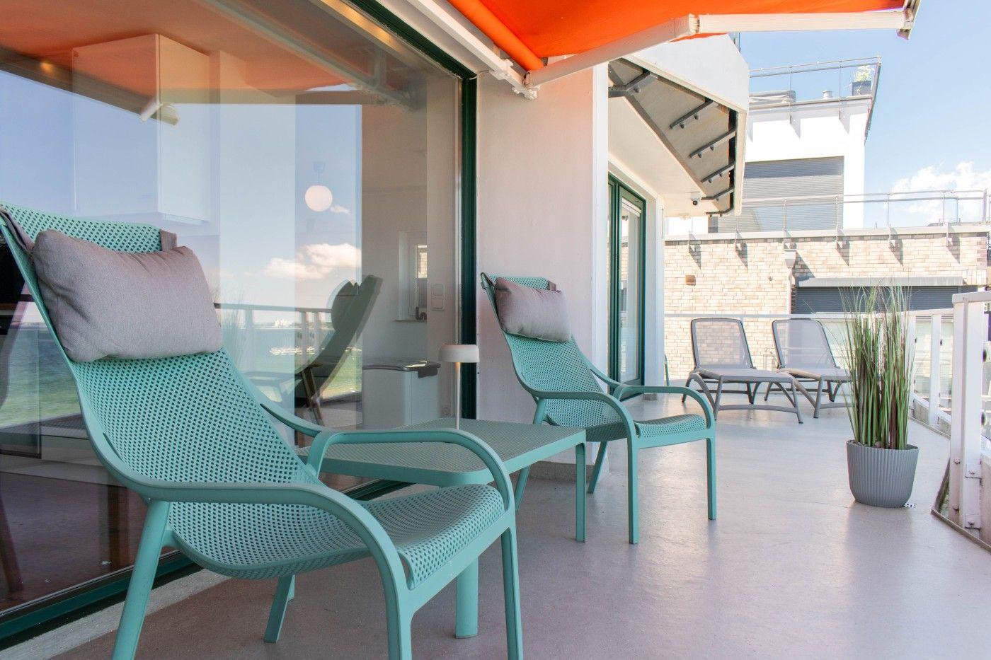 Terrasse mit zwei mintgrünen Liegestühlen, orangefarbenem Markisenüberdachung und Pflanze.