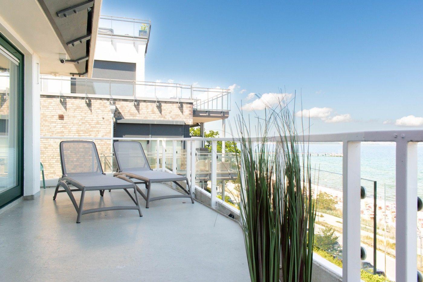 Terrasse mit zwei Liegestühlen und Meerblick. Hintergrund: Strand und blaues Wasser.