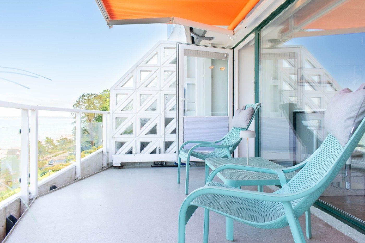 Terrasse mit zwei hellblauen Stühlen und orangefarbenem Sonnenschutz. Blick auf den Himmel und die Umgebung.