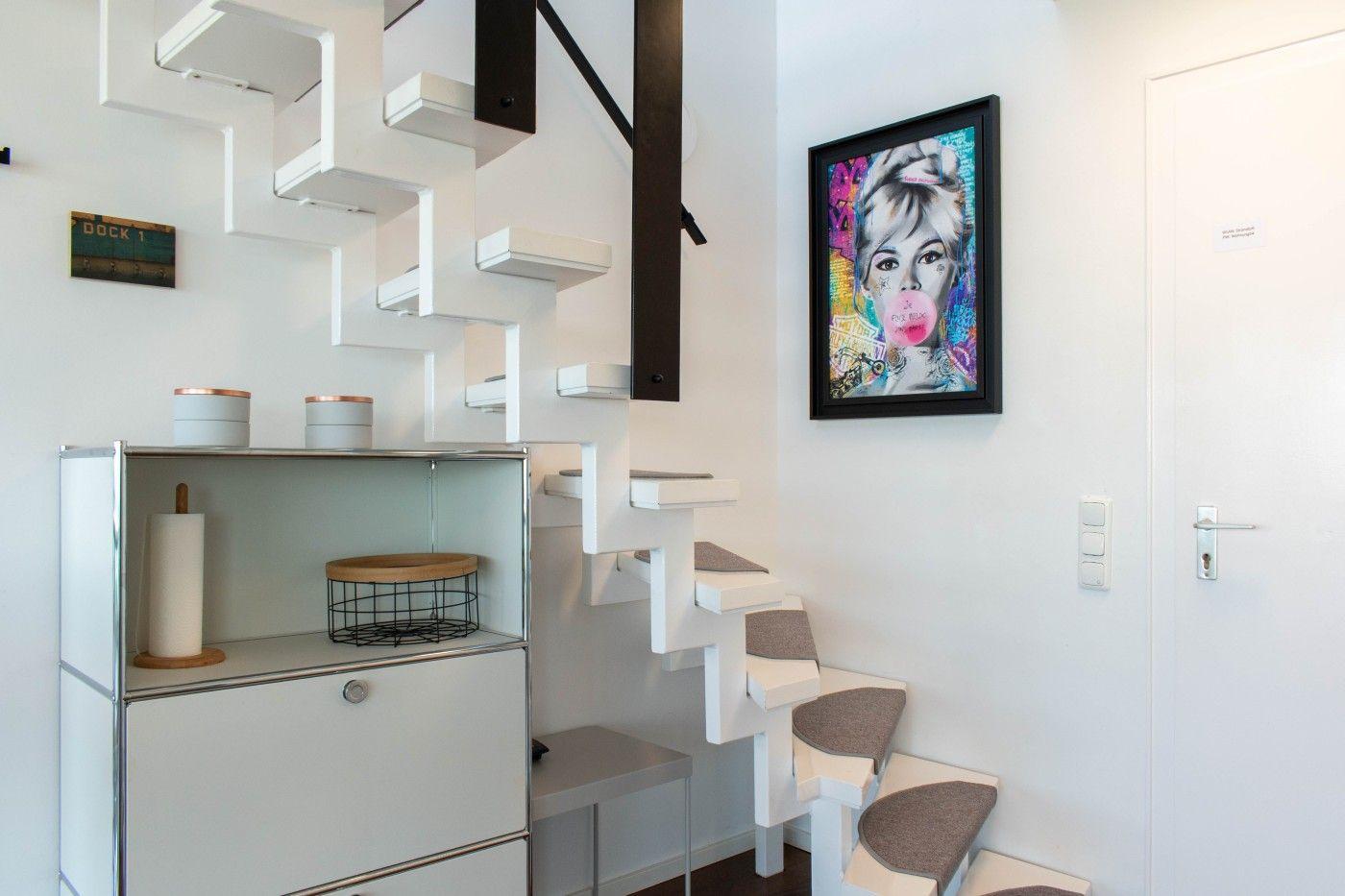 Treppenhaus mit weißer Treppe, Kunstwerk an der Wand und Metallregal mit Aufbewahrung.