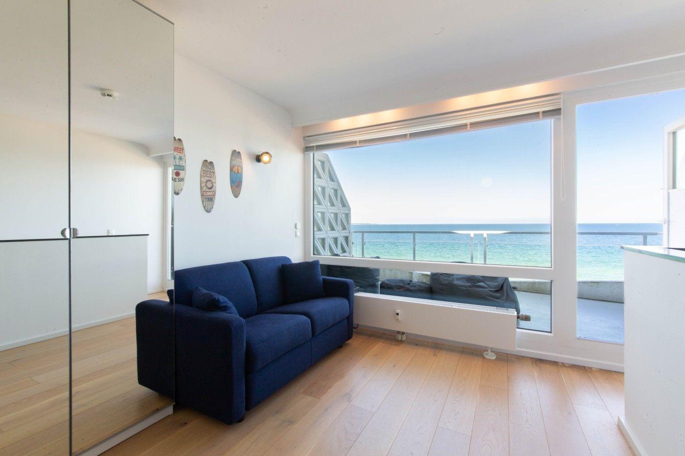 Ein Wohnzimmer mit blauem Sofa und Blick auf das Meer.