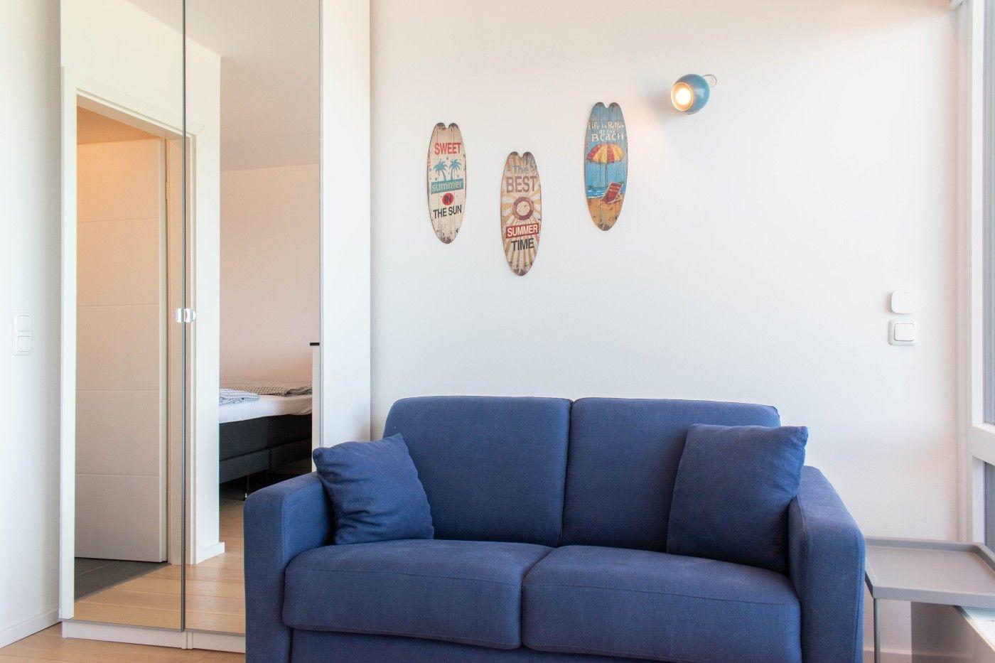 Blauer Sofa im Wohnbereich mit drei Surfboard-Decorations an der Wand. Durchgang zur Schlafzimmer.