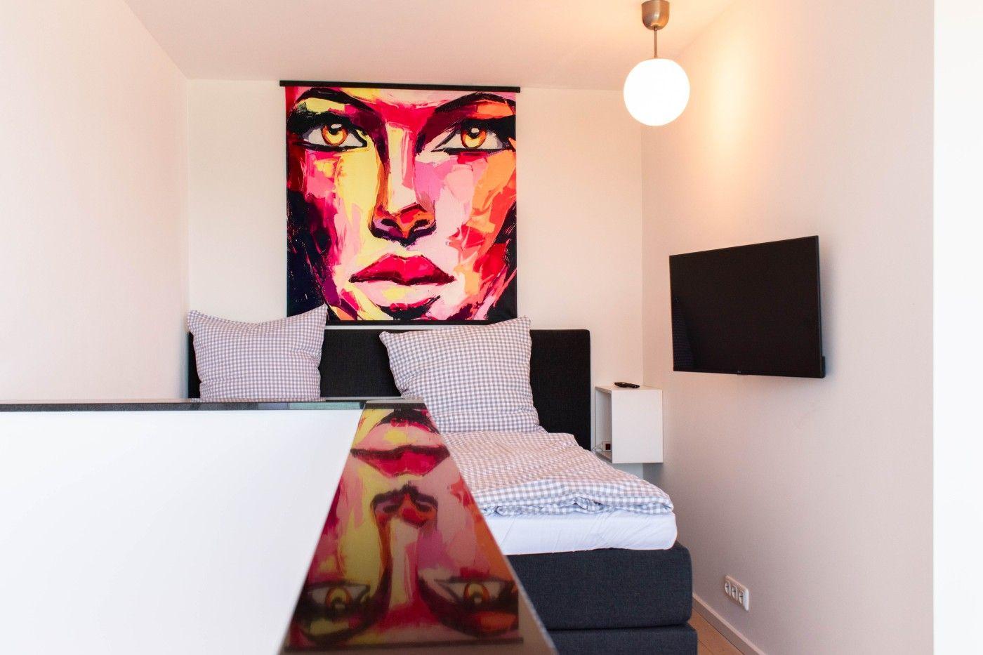Schlafzimmer mit Bett, Wandbild und Fernseher an der Wand.