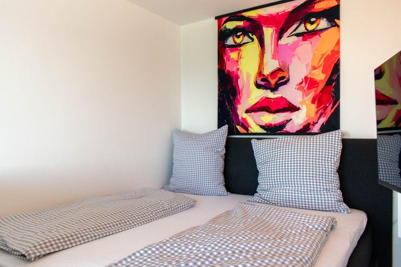 Ein Bett mit karierten Kissen und Decke, an der Wand hängt ein großes Porträt.