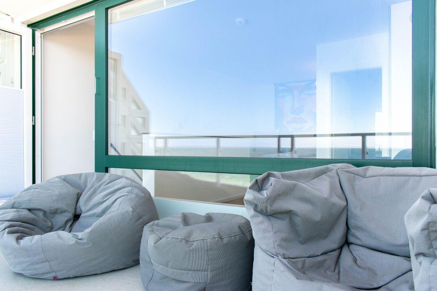 Große Fenster mit Blick auf den Strand. Graue Sitzkissen und ein kleiner Tisch.