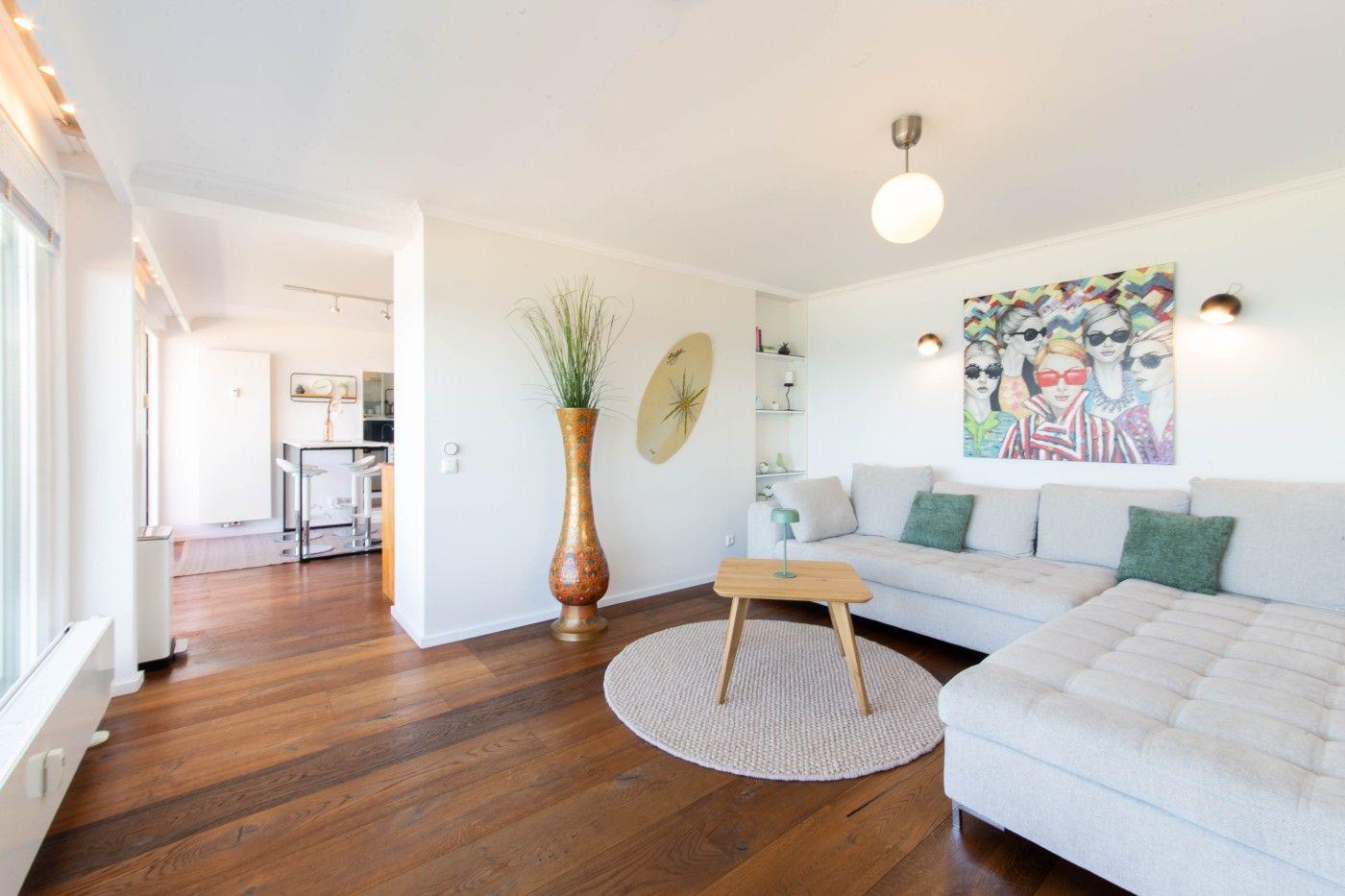 Wohnzimmer mit Sofa, Tisch und Wandbild. Holzboden und helle Wände.