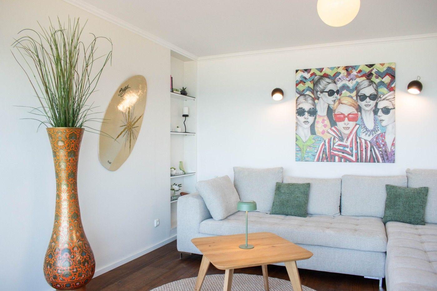 Wohnzimmer mit Sofa, Tisch und Wandbild. Großer Vasen mit Pflanze und Dekoration.