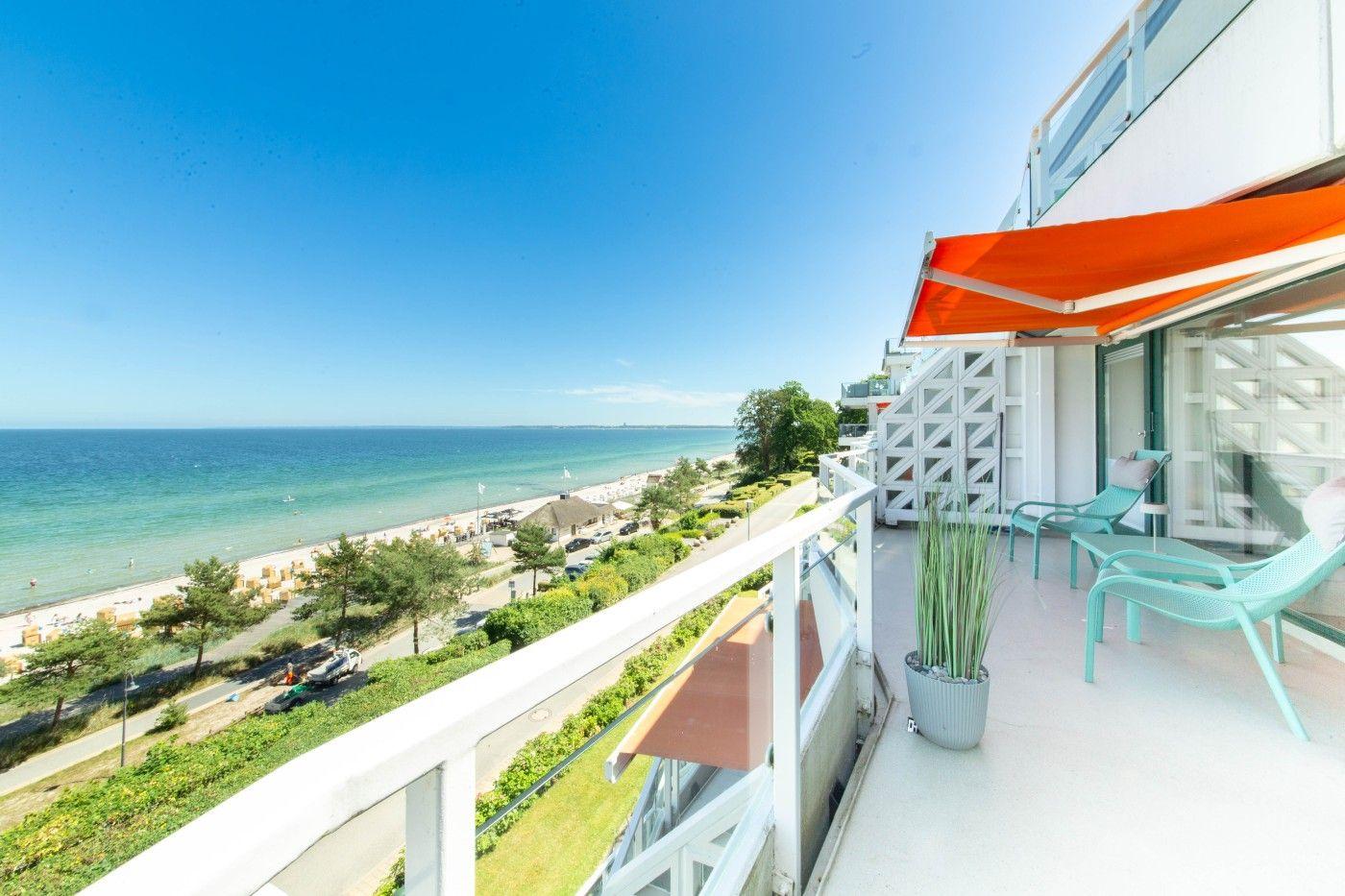 Terrasse mit Blick auf Strand und Meer. Liegestühle und orangefarbener Sonnenschutz.