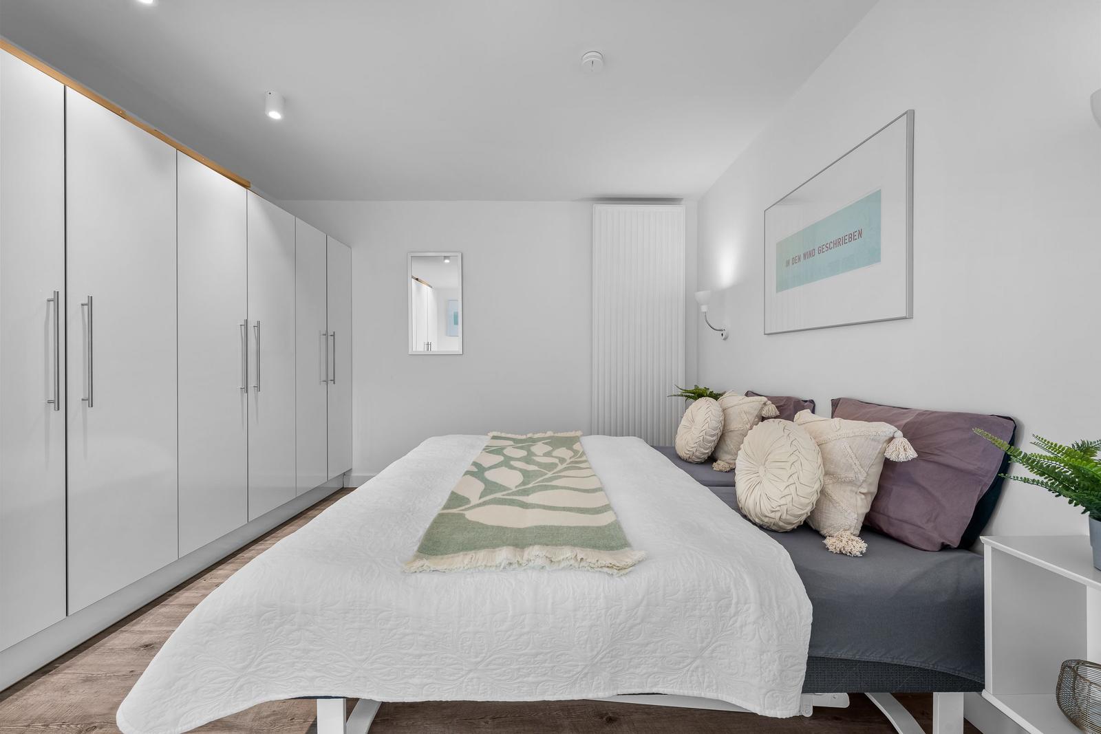 Schlafzimmer mit Bett, Kleiderschrank und Wandbild.