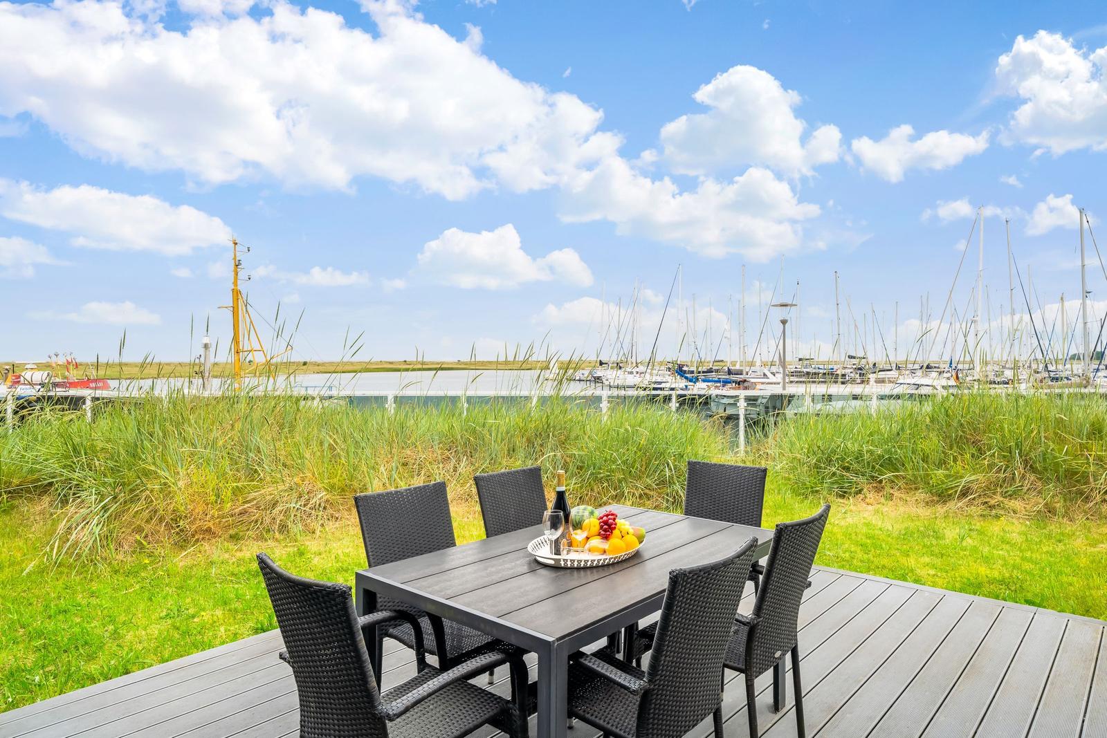 Terrasse mit Tisch und Stühlen, Blick auf Hafen mit Booten und Gras.