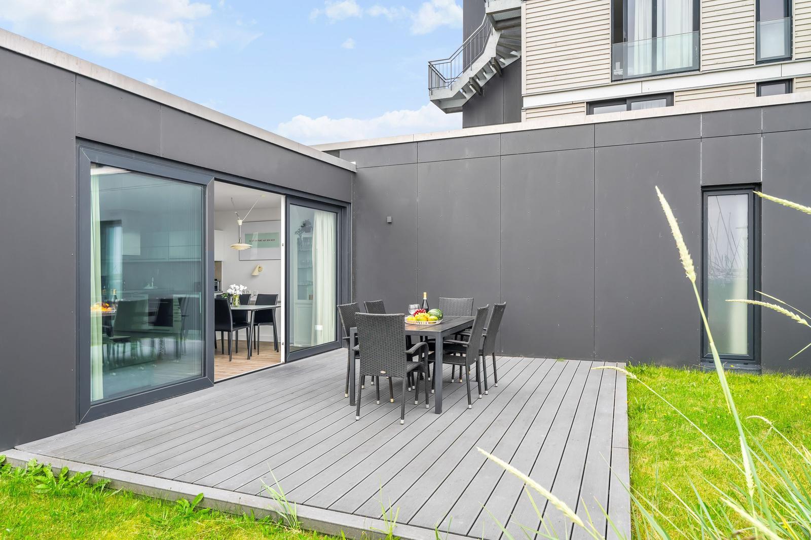 Terrasse mit Tisch und Stühlen, angrenzende Küche und modernes Gebäude.