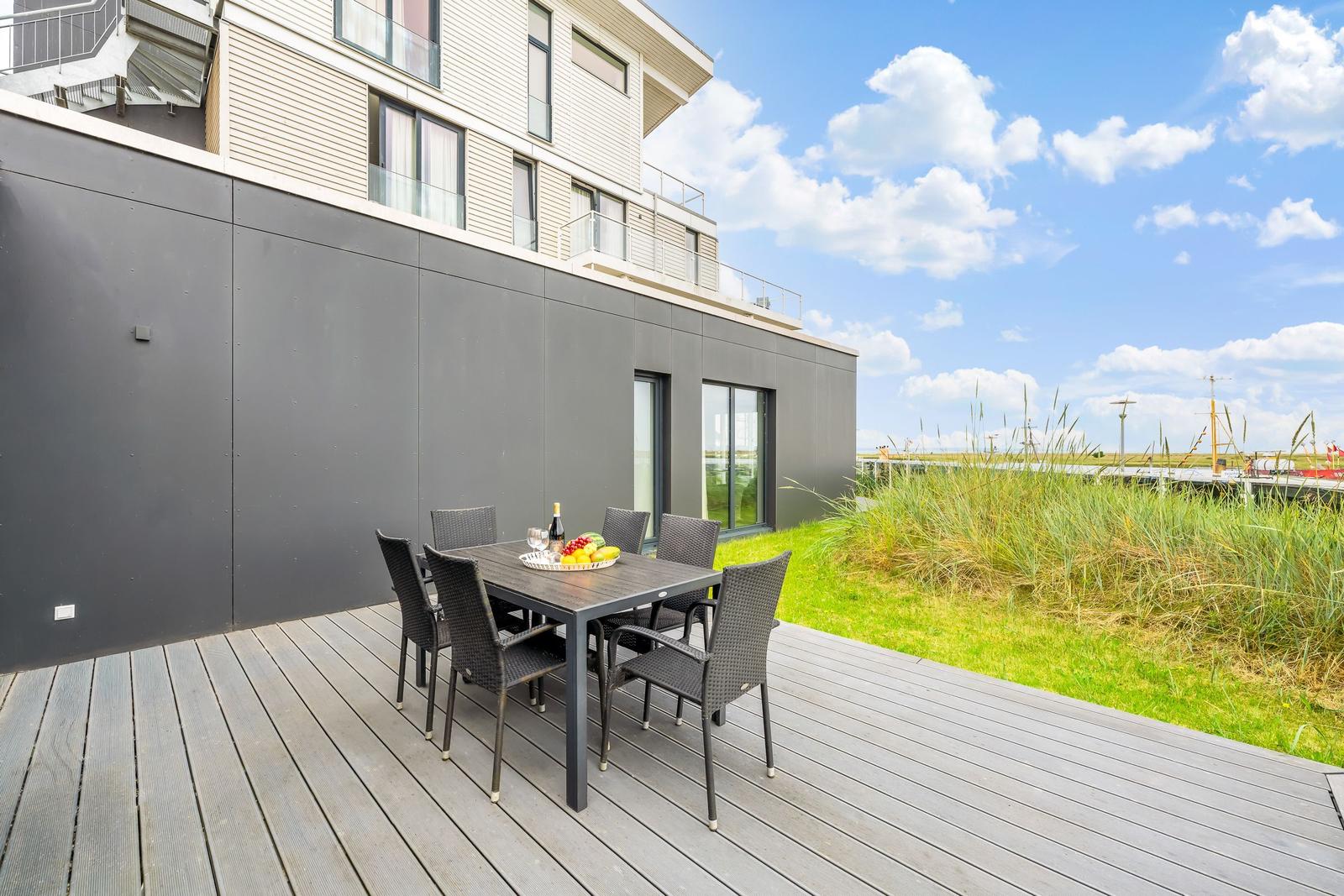 Terrasse mit Tisch und Stühlen, Blick auf Gras und Himmel.