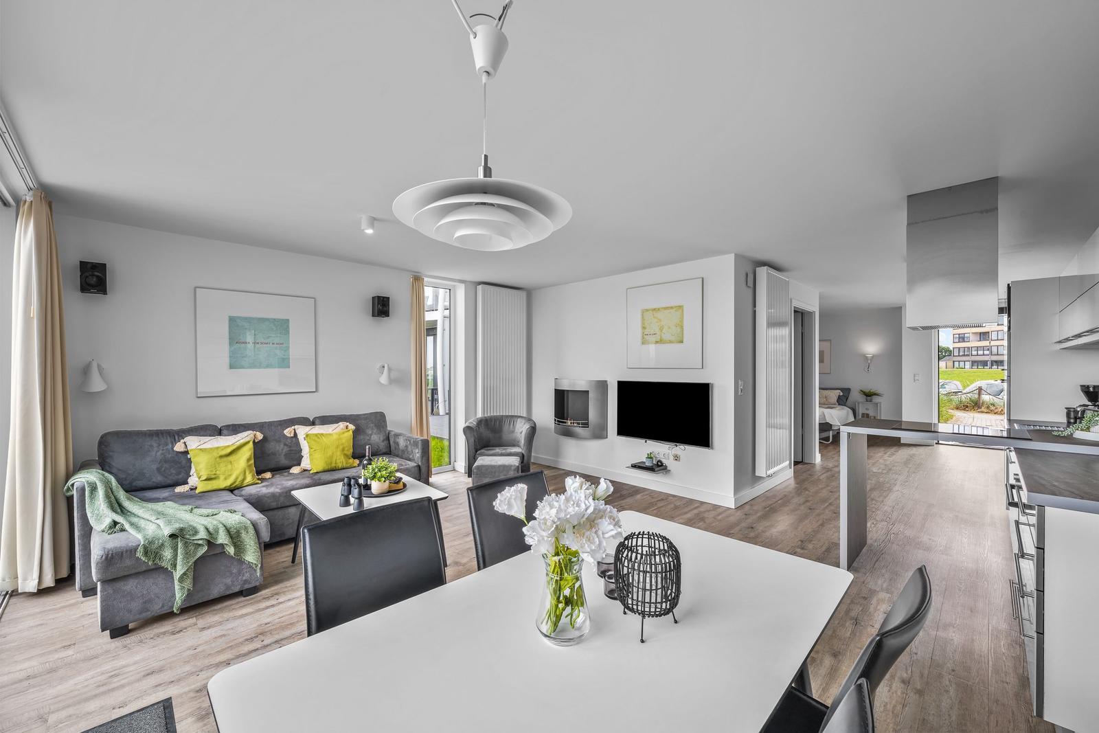 Wohn- und Essbereich mit Sofa, TV und Küchenzeile. Holzboden und modernes Design.