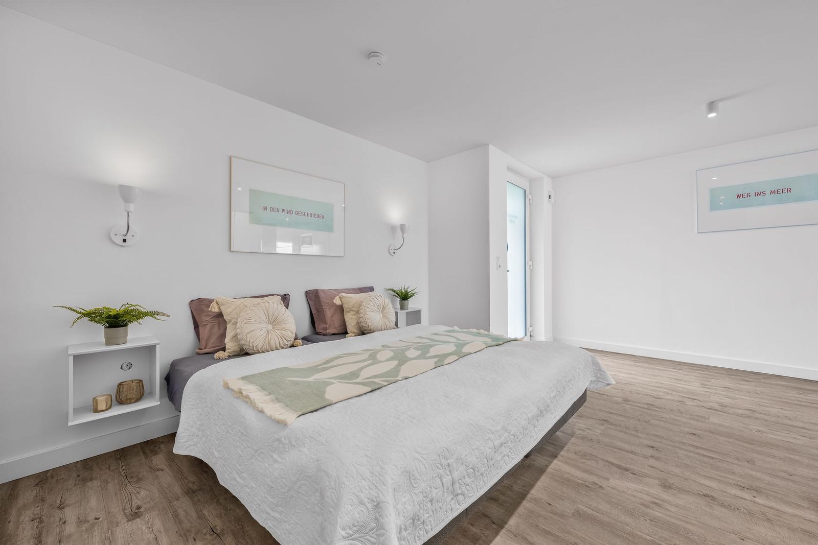 Schlafzimmer mit Bett, Wandbildern und Holzboden.