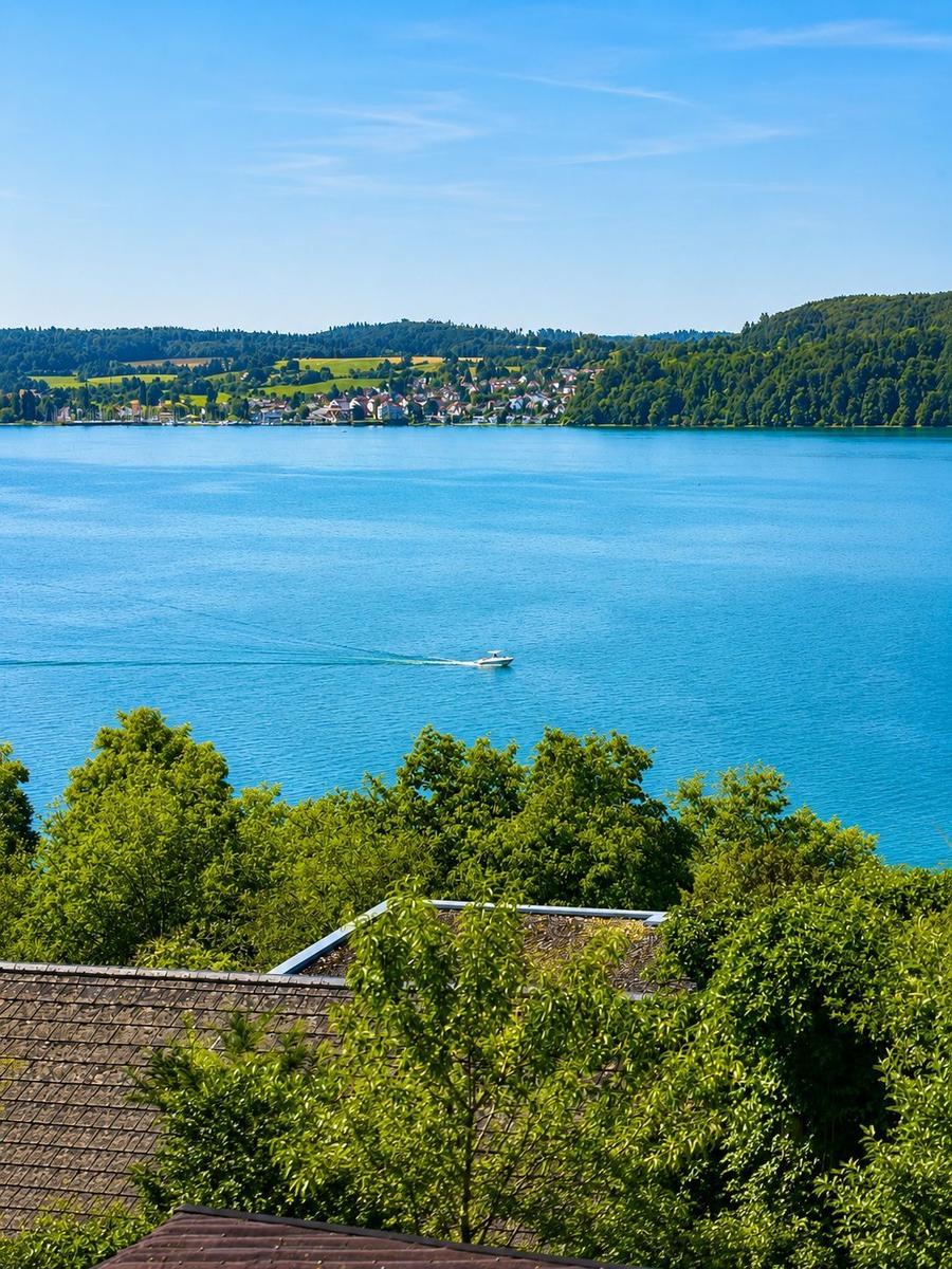Weitläufiger Blick auf einen See mit Boot und grünen Hügeln im Hintergrund.
