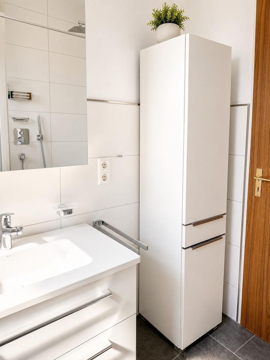 Badezimmer mit Waschbecken, Spiegel und Hochschrank. Pflanze auf dem Schrank.