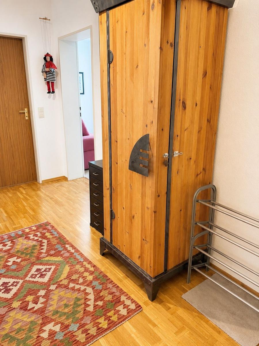 Holzschrank mit Metallbeschlägen, Teppich und Kleiderständer im Raum.