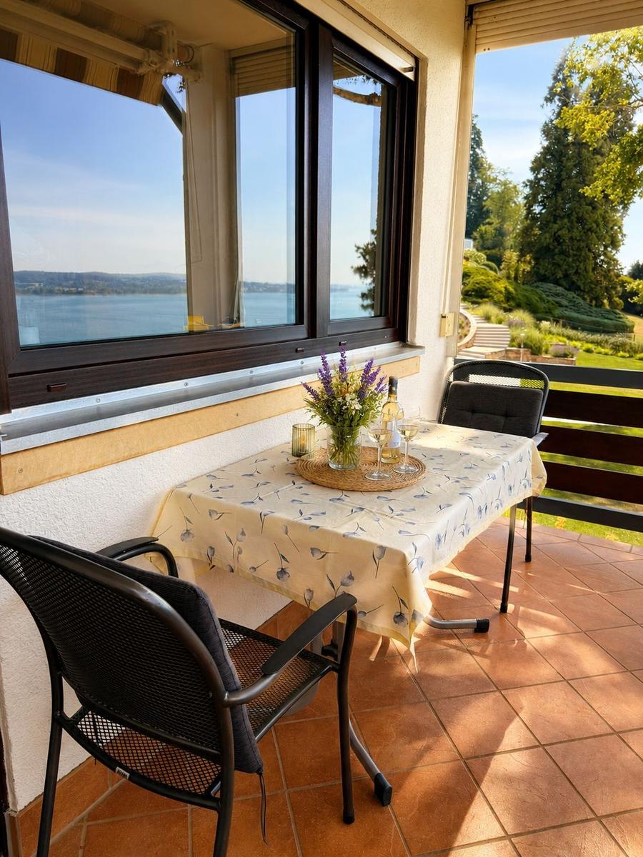Terrasse mit Tisch, Stühlen und Blick auf See und Garten.